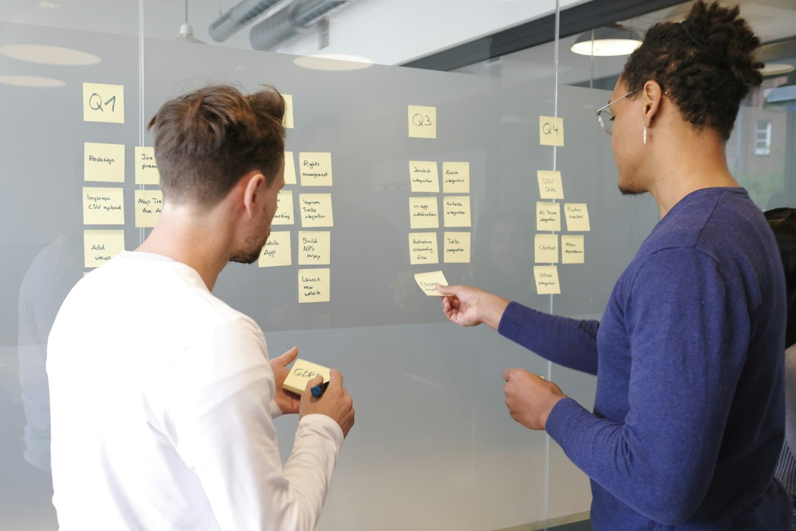 Two colleagues mapping out a process with sticky notes on a glass wall.
