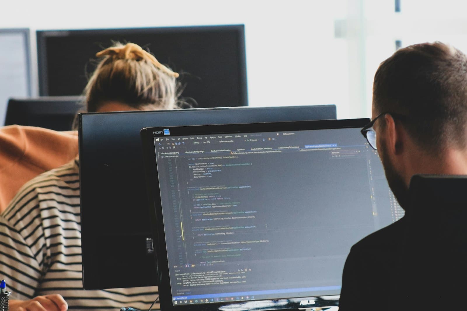 Two developers working on code at their monitors in a modern office.