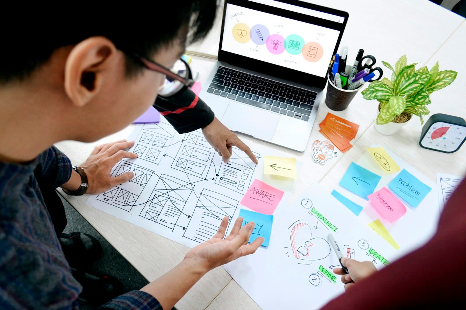 Designer sketching website wireframes on paper beside a laptop.